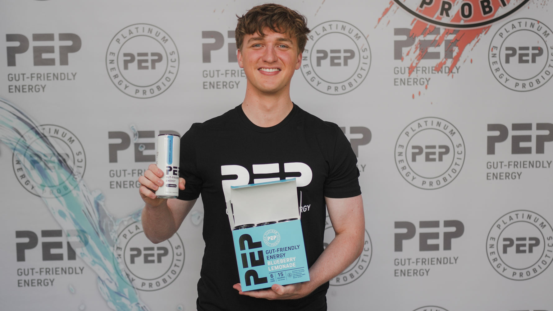Luke Beasley holding a can of 'PEP' and a 6-pack carton of PEP against a PEP-branded background