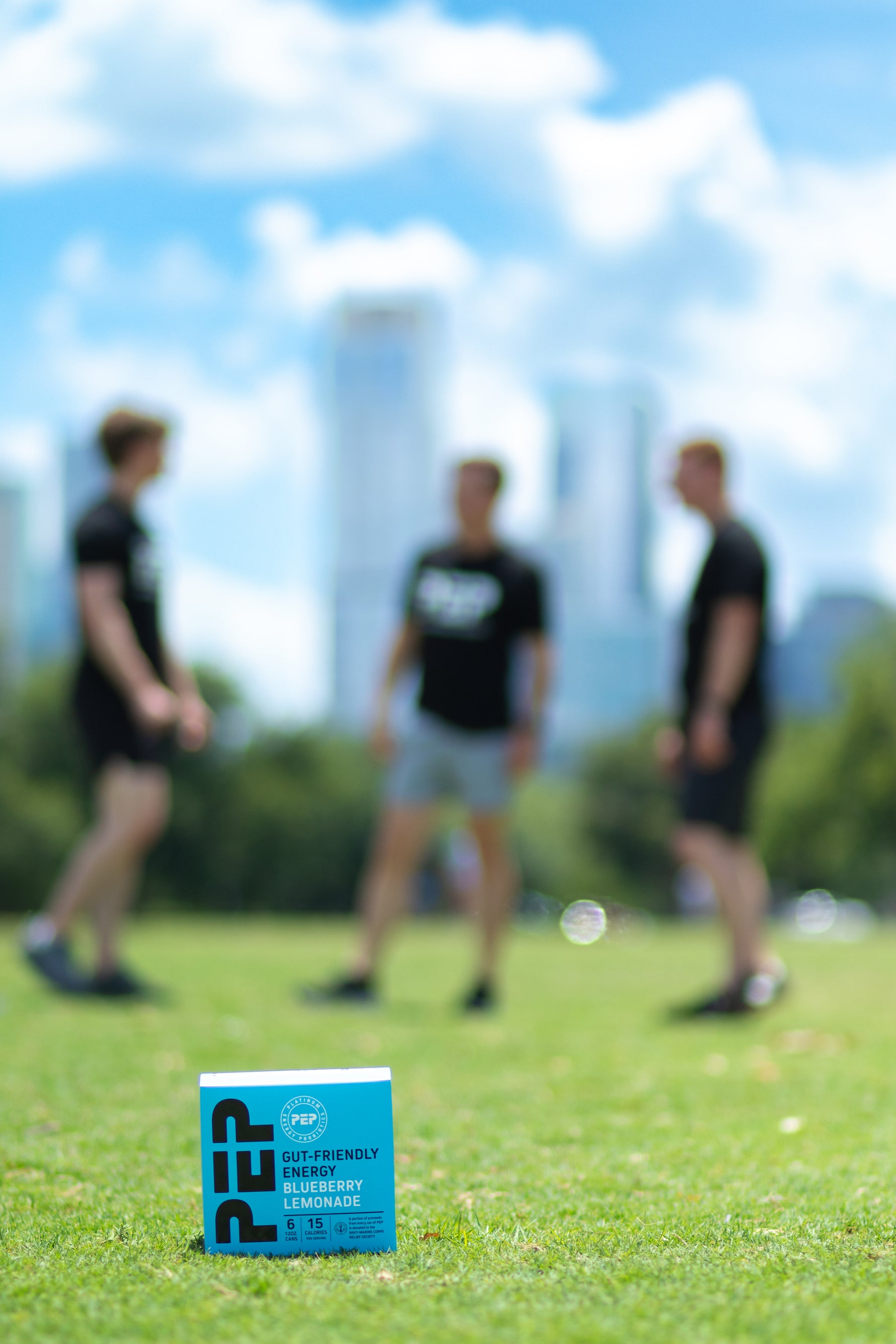 The three Beasley brothers in a park out of focus with a 6-pack carton of PEP Blueberry Lemonade in focus in the foreground.