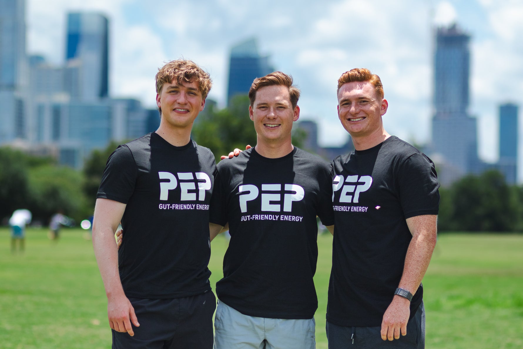 The Beasley brothers wearing black 'PEP' t-shirts standing in a park with the Austin city skyline in the background.