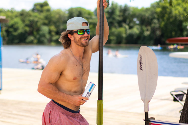 Man holding a paddle and a can of PEP Gut-Friendly Energy on a dock with a lake and trees in the background