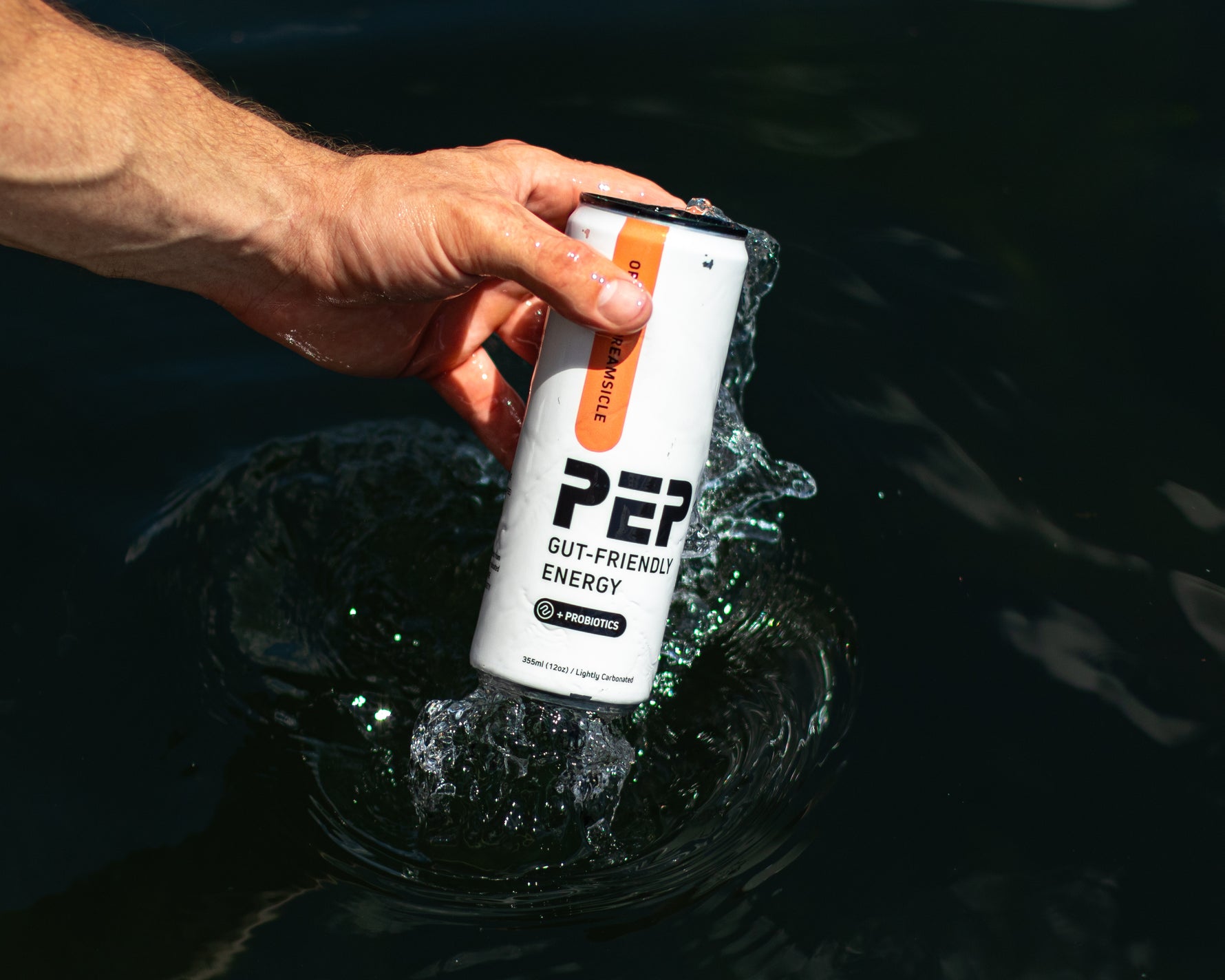 Hand holding a can of PEP Gut-Friendly Energy drink over water